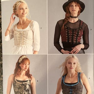 May include: A sewing pattern for four different corset tops. The pattern is called Simplicity Costumes R11853. The corsets are shown in different colors and fabrics, including a black and white floral print, a red and black striped fabric, a beige fabric with lace, and a blue and black tweed fabric.