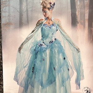 Puede incluir: Un patrón de costura Simplicity que muestra un vestido de fantasía azul claro con mangas transparentes y detalles florales. El vestido tiene una falda en capas, adecuado para cosplay o eventos de disfraces. La modelo lleva un tocado a juego.