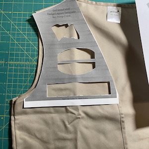 May include: A tan Girl Scout vest with a printed badge layout template. The template includes spaces for badges, a troop crest, and a Girl Scout logo. The text on the template reads "Girl Scout Vest Badge Layout Template No Troop Crest" and "Night Owl Quilts TX - Sarah Yates".