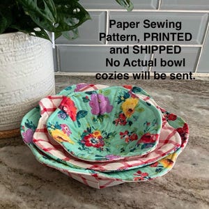 May include: Three nesting bowl cozies in a floral pattern. The largest cozy is red and white gingham, the middle cozy is green with a floral pattern, and the smallest cozy is a solid green color. The cozies are on a brown countertop. Paper Sewing Pattern, PRINTED and SHIPPED. No Actual bowl cozies will be sent.