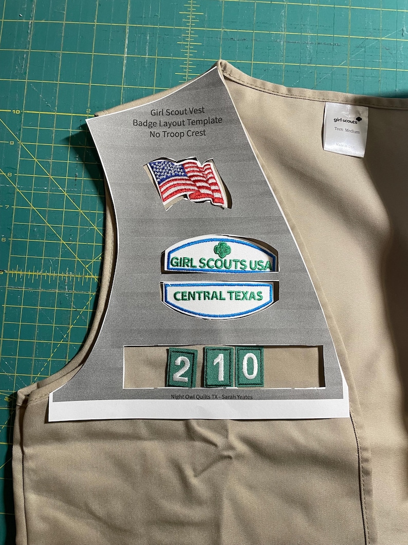 May include: A tan Girl Scout vest with a badge layout template. The template includes a space for the American flag, a Girl Scouts USA patch, a Central Texas patch, and a number patch. The text "Girl Scout Vest Badge Layout Template No Troop Crest" is printed on the template. The text "girl scouts Tem Medium" is printed on the vest.
