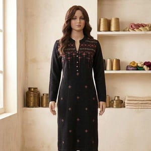 Peut inclure: Une tunique noire à manches longues dotée d'une patte de boutonnage au niveau de l'encolure et d'un motif géométrique répétitif dans des tons rouge, blanc et doré. Le vêtement présente une coupe droite avec de petits motifs losanges brodés.