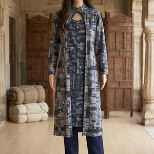 Peut inclure: Une veste longue à manches longues arrivant au genou avec un motif géométrique gris foncé et bleu, portée sur un haut sans manches assorti à encolure goutte d'eau et un pantalon bleu marine uni. L'ensemble présente un imprimé abstrait uniforme.
