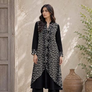 Peut inclure: Une tunique à manches longues avec un panneau à motif léopard noir et blanc sur le devant et le dos, contrasté par des manches noires unies et une sous-couche noire unie. La tunique présente un col en V, une patte de boutonnage et des poignets léopard.