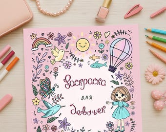 Op de afbeelding: Een roze kleurboek met de tekst "Раскраска для Девочек" omringd door kleurrijke illustraties van een regenboog, vogels, bloemen, een zon, een heteluchtballon en een meisje. Markers, potloden en accessoires zijn rond het boek gerangschikt.
