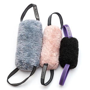 Pu&ograve; includere: Tre giocattoli di peluche per cani in grigio, rosa e nero. Ogni giocattolo ha un'impugnatura ad anello e un'etichetta con la scritta "GIFTS FOR TAILS". I giocattoli sono cilindrici e realizzati in un materiale morbido e strutturato.
