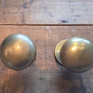 May include: Two spherical door knobs made of polished brass with a smooth, reflective surface. Each knob features a rounded, ball-shaped handle attached to a circular base plate, showcasing a warm, metallic gold tone and a consistent finish.