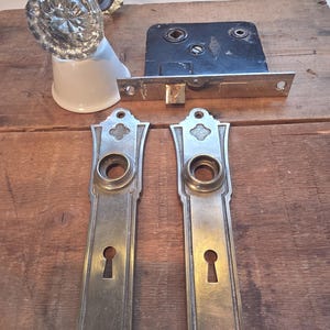 Peut inclure: Un ensemble de quincaillerie de porte comprenant deux plaques métalliques allongées avec entrées de serrure, un mécanisme de serrure à mortaiser noir et un bouton de porte en verre facetté transparent sur base argentée et support en céramique.