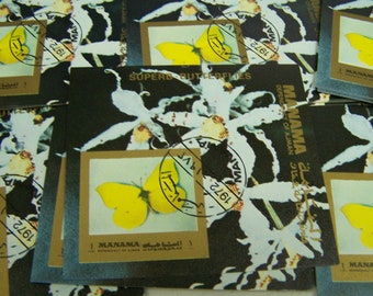 May include: A collection of vintage postage stamps featuring butterflies and orchids. The stamps are from the 1972 "Superb Butterflies" series issued by the Dependency of Ajman, Manama. The stamps are in various shades of yellow, white, and black.