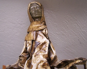 Può includere: Una scultura in cartapesta di una persona che indossa una tunica marrone e bianca. La scultura ha un viso dettagliato con un'espressione neutra.