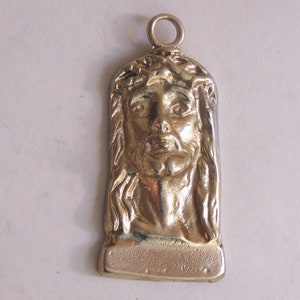 May include: A gold-toned pendant featuring a detailed relief sculpture of Jesus Christ's face with a crown of thorns.