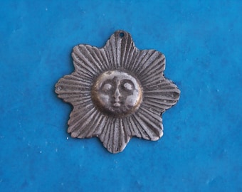 May include: A silver sun charm with a face and rays. The charm is on a blue background.