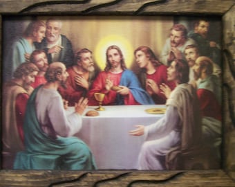 May include: A framed print depicting the Last Supper. The artwork features Jesus at the center, surrounded by his disciples, seated around a white table. The frame is made of dark wood with a textured, carved design.