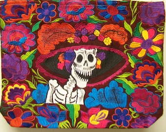 May include: A brown tote bag with colorful embroidered flowers and a skeleton wearing a hat. The skeleton is smiling and has a white skull with black eyes.