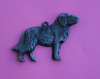 May include: A silver metal dog charm with a detailed design. The dog is standing on all four legs with its head turned to the side. The charm has a loop at the top for attaching to a necklace or bracelet.