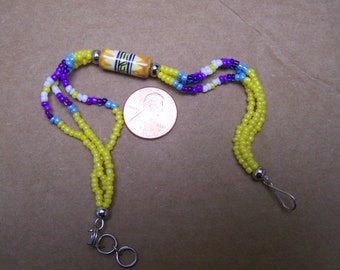 May include: A yellow beaded bracelet with a colorful ceramic bead and silver clasps. The bracelet is next to a US penny for size comparison.