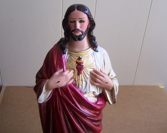 May include: A white and red statue of Jesus Christ with a gold heart on his chest. The statue is painted with realistic details and has a sorrowful expression.
