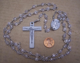May include: A silver rosary with clear glass beads, a silver crucifix with a figure of Jesus Christ, and a silver medal with a depiction of the Virgin Mary.