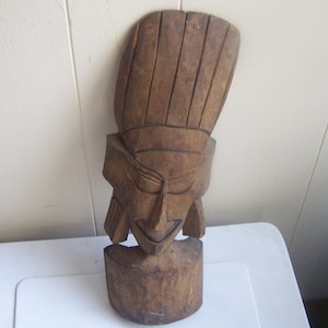 May include: A wooden carved mask with a tall, pointed headpiece. The mask has a stylized face with closed eyes and a wide mouth.
