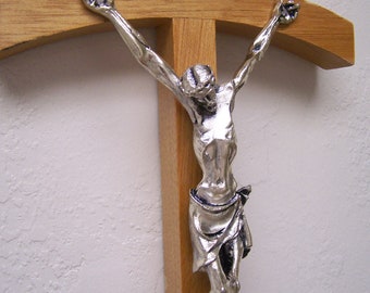 May include: A silver-colored Jesus figure on a wooden cross. The figure is depicted with outstretched arms and a crown of thorns.