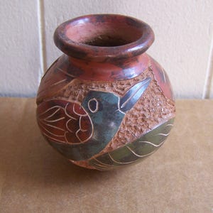 May include: A small, round, terracotta vase with a textured surface. The vase is decorated with a colorful bird design in shades of red, blue, green, and brown.