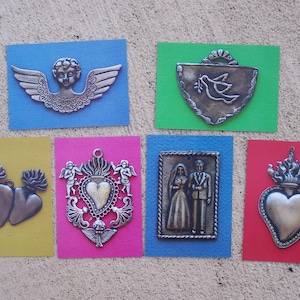May include: Six silver-toned metal religious ornaments on colorful backgrounds. The ornaments include a cherub with wings, a dove in a shield, two hearts with flames, a heart with a flame and a crown, and a couple standing together.