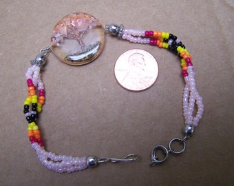 May include: A beaded bracelet with a pink, orange, yellow, and black color scheme. The bracelet features a round pendant with a tree of life design inside. The pendant is approximately the size of a US penny.