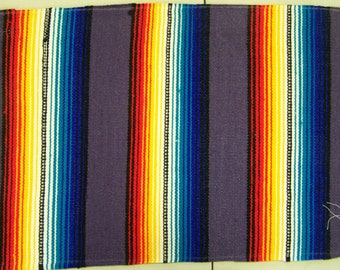 May include: A purple woven rug with colorful stripes in red, orange, yellow, white, blue, and black. The rug has a fringe border.