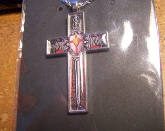 May include: A silver cross pendant with a red and white shield design. The shield has a sword and a crown on it. The cross is on a black background.