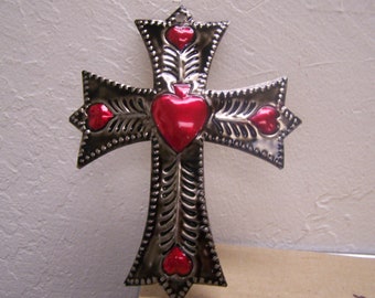 May include: A silver metal cross with red heart accents. The cross is decorated with a beaded border and intricate designs.