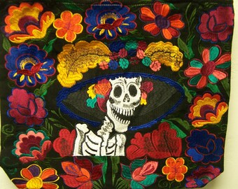 May include: Black tote bag with colorful embroidered flowers and a skeleton wearing a hat with flowers. The skeleton is smiling and has a white skull.