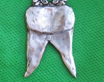 May include: A silver tooth charm with an ornate design at the top. The charm is shaped like a tooth and has a hole in the top for hanging.