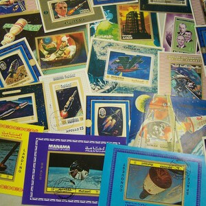 May include: A collection of vintage postage stamps featuring space exploration themes. The stamps showcase rockets, astronauts, and celestial bodies, with text in English and Arabic. Various colors and designs are visible, including stamps from Manama and Ajman.
