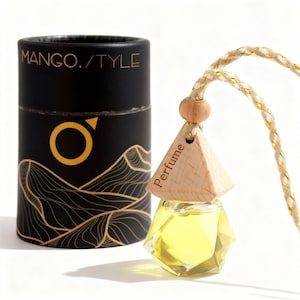 May include: A black cylindrical container and a perfume bottle. The container has the text "MANGO./TYLE" and a gold logo. The perfume bottle is a geometric shape with a wooden top and a yellow liquid inside. The bottle hangs from a gold and beige rope.