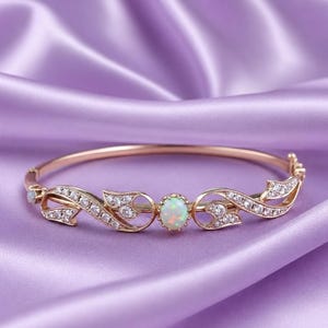 May include: A rose gold hinged bangle bracelet featuring a central oval-cut opal gemstone surrounded by small clear stones. The metal band is decorated with intricate swirling leaf-like patterns encrusted with tiny sparkling white stones.