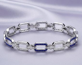 May include: A silver-toned link bracelet featuring a repeating geometric pattern. Each rectangular link is accented with small, clear white stones and vibrant blue stones set along the edges, creating a continuous, structured design.