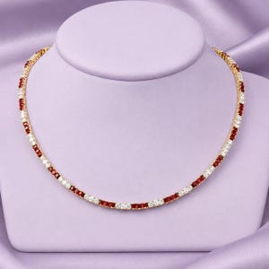 May include: A gold-toned necklace featuring an alternating pattern of rectangular-cut red stones and clear white stones. The stones are set in a continuous row, creating a vibrant, symmetrical design that encircles the neck in a classic style.