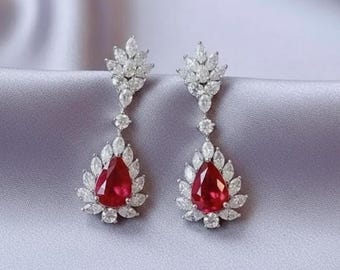 May include: A pair of drop earrings featuring a central pear-shaped red gemstone surrounded by a halo of small, clear, marquise-cut stones. Above the pear-shaped section, a cluster of marquise-cut stones forms a leaf-like design element.