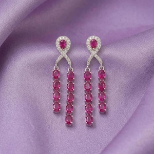 May include: A pair of silver-toned drop earrings featuring a teardrop-shaped top set with a small pink stone, surrounded by clear pavé crystals. Each earring has two dangling chains of oval-cut pink stones, creating a symmetrical, tiered design.