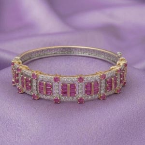 May include: A hinged bangle bracelet crafted from gold and silver-toned metal, featuring a repeating pattern of rectangular-cut vibrant pink rubies and small, clear round-cut white stones set in a structured, multi-layered geometric design.
