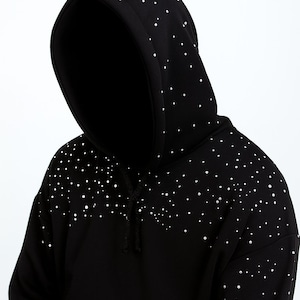 Puede incluir: Sudadera con capucha negra con adornos de puntos blancos, con el texto "FITLOYAL" en la parte superior. La sudadera tiene un cordón y una pequeña etiqueta roja. Los puntos se concentran alrededor de los hombros y la capucha.