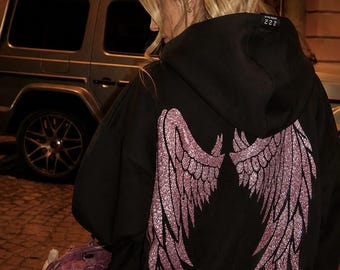 May include: A black hooded sweatshirt featuring a large, glittery pink wing graphic on the back. The hoodie includes a small black label on the collar with the number 222 and a logo in the upper right corner that reads FL FIT LOYAL.