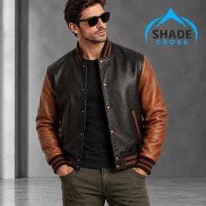 May include: A varsity-style jacket featuring a black leather body, brown leather sleeves, and a ribbed collar and cuffs with brown and black stripes. The jacket has a snap-button front closure and two side pockets. The text SHADE CROSS is visible.