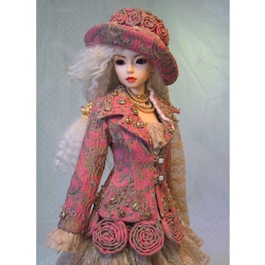 May include: A doll wearing a pink and gold patterned jacket with gold embellishments and a matching hat. The doll has long, white hair and is adorned with a pearl necklace. The jacket features rose-shaped details at the waist. The doll is wearing a dress with lace sleeves.