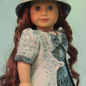 May include: A doll wearing a light blue and white dress with a beaded jacket and a light blue hat with a white bow. The doll has long red hair and blue eyes.