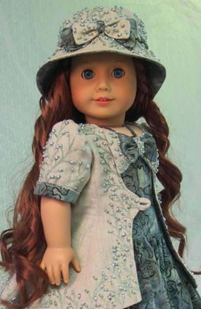 May include: A doll wearing a light blue and white dress with a beaded jacket and a light blue hat with a white bow. The doll has long red hair and blue eyes.