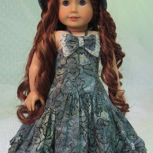 May include: A doll wearing a blue and white floral dress with a matching blue and white hat. The doll has long brown hair and blue eyes.