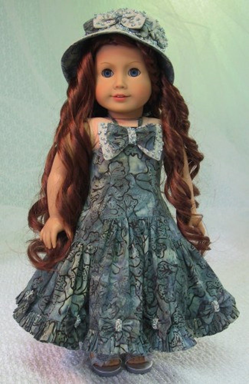 May include: A doll wearing a blue and white floral dress with a matching blue and white hat. The doll has long brown hair and blue eyes.