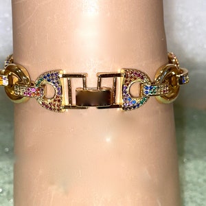 May include: A gold chain bracelet with a clasp closure. The chain is decorated with colorful cubic zirconia stones.