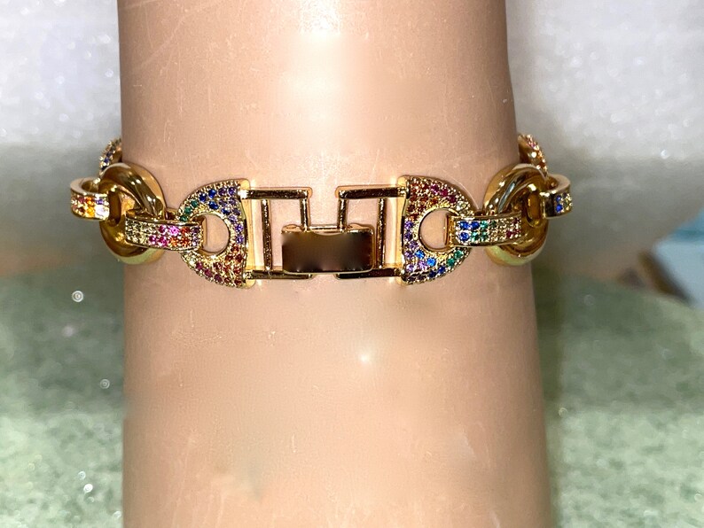 May include: A gold chain bracelet with a clasp closure. The chain is decorated with colorful cubic zirconia stones.